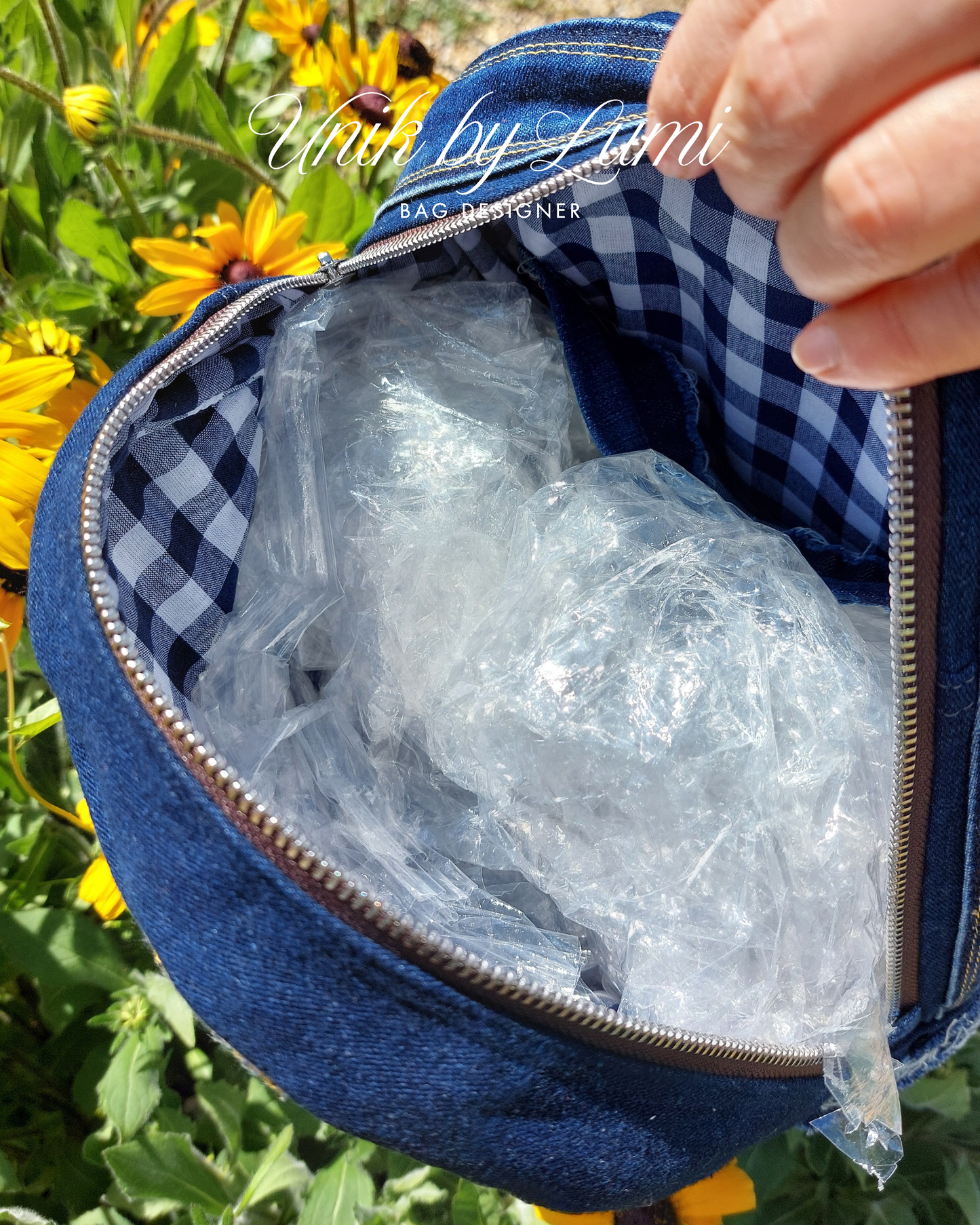 Blue backpack with a checkered interior, containing clear plastic wrap, against a natural background with yellow flowers.