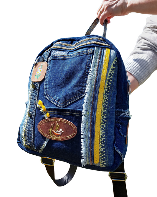 Blue denim backpack with yellow accents held by a person on a white background